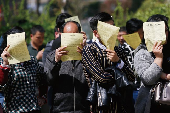 Chinese businessman that are part of a business cult line up while blocking their faces with paper.