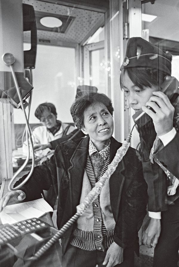 A couple Tianjin women in a phone booth experiencing how to use a telephone.