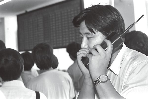 A Chinese man covering his mouth while speaking on a large mobile phone.